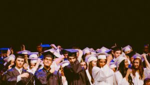 Image of students at their graduation in their robes reaching for their mortar board hats to throw up in the air